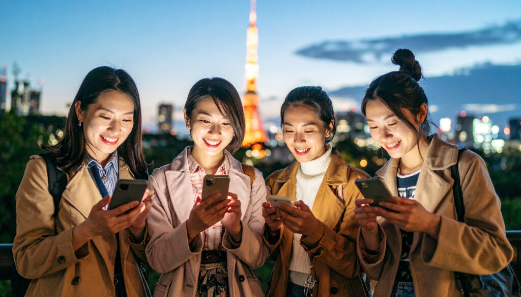 夕暮れの東京でスマートフォンを見る女性4人組